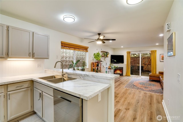 kitchen with stainless steel dishwasher, a peninsula, light countertops, and a sink