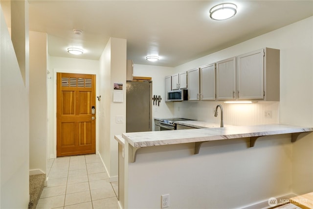 kitchen with a kitchen bar, light countertops, light tile patterned floors, a peninsula, and stainless steel appliances