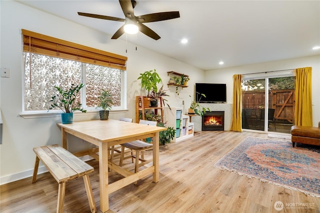 dining room with baseboards, ceiling fan, a lit fireplace, recessed lighting, and light wood-style floors