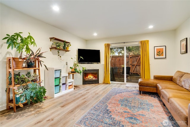 living area featuring recessed lighting, a warm lit fireplace, and wood finished floors