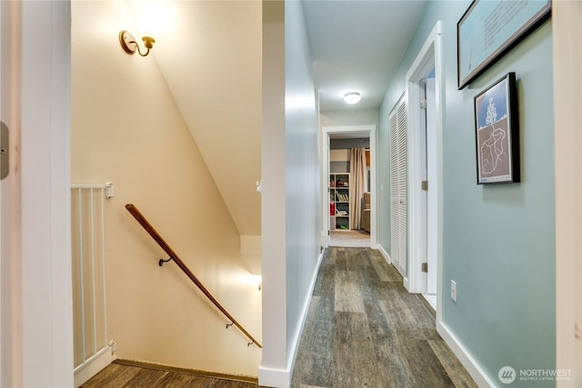 hallway with baseboards, an upstairs landing, and dark wood finished floors