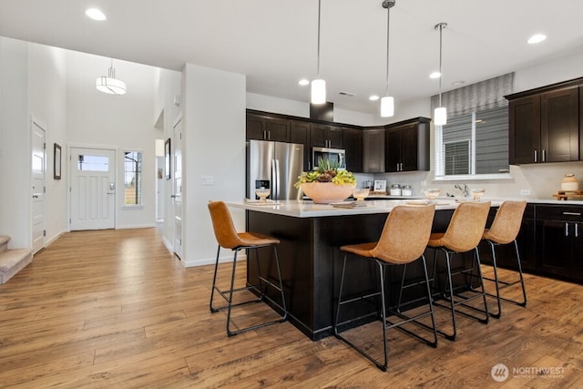 kitchen featuring stainless steel appliances, a breakfast bar, light countertops, light wood-type flooring, and a center island