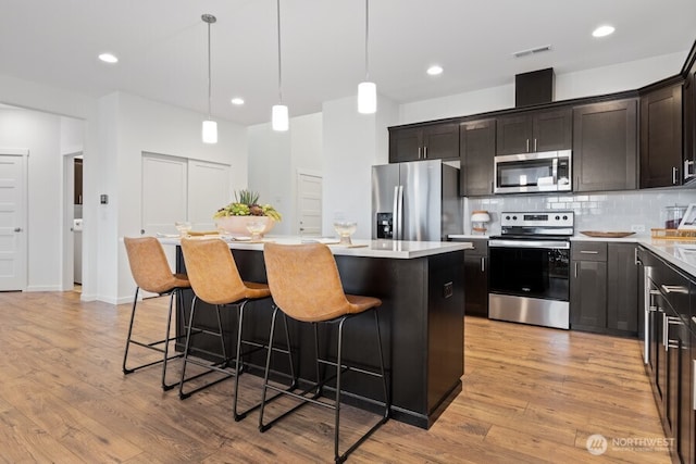 kitchen featuring appliances with stainless steel finishes, a center island, light wood-type flooring, and decorative backsplash