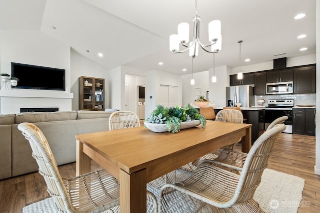 dining space featuring a notable chandelier, a fireplace, recessed lighting, vaulted ceiling, and light wood-type flooring