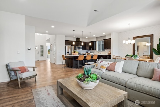 living area with a notable chandelier, recessed lighting, visible vents, vaulted ceiling, and light wood-type flooring