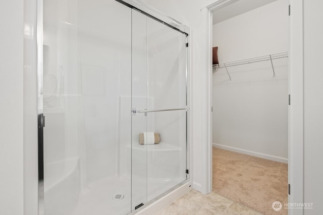 full bath with a spacious closet, a stall shower, and baseboards