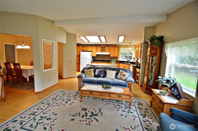 living room with baseboards, vaulted ceiling with skylight, light wood-style floors, and an inviting chandelier