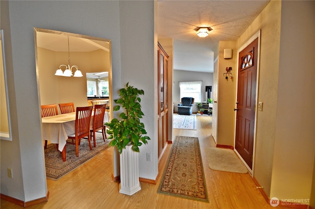 hallway featuring light wood finished floors, baseboards, and a notable chandelier