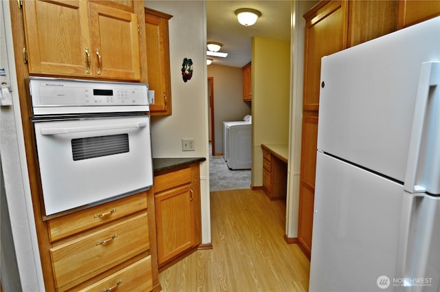 kitchen with white appliances, dark countertops, brown cabinets, light wood-style floors, and washing machine and dryer