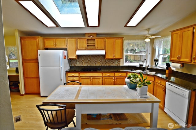 kitchen featuring vaulted ceiling with skylight, under cabinet range hood, white appliances, a sink, and visible vents