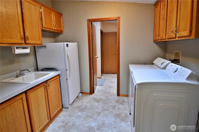 laundry area featuring cabinet space, baseboards, light floors, washing machine and dryer, and a sink