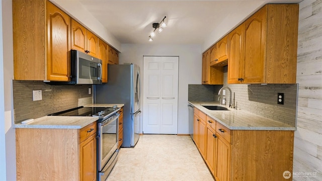 kitchen featuring light stone countertops, a sink, decorative backsplash, stainless steel appliances, and brown cabinets