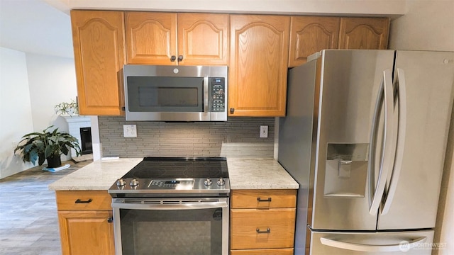 kitchen featuring light stone counters, backsplash, appliances with stainless steel finishes, and light wood-style flooring