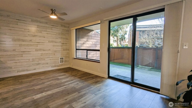 unfurnished room with baseboards, wooden walls, wood finished floors, and a ceiling fan