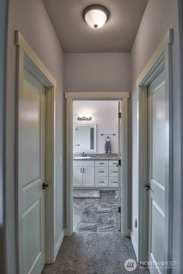 hallway with carpet flooring, a sink, and baseboards