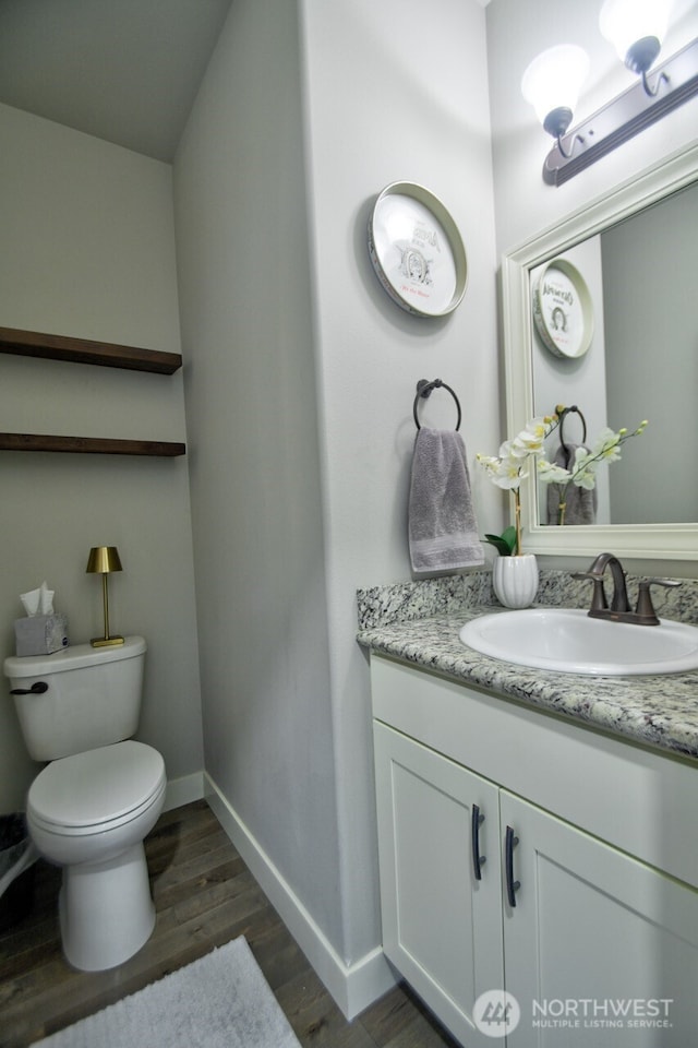 half bath featuring baseboards, vanity, toilet, and wood finished floors