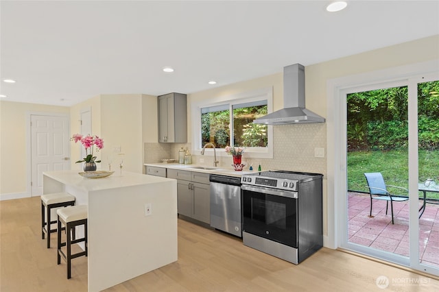 kitchen with stainless steel appliances, a breakfast bar, a sink, wall chimney range hood, and gray cabinets