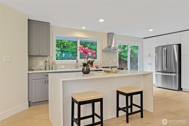 kitchen featuring a kitchen bar, gray cabinetry, freestanding refrigerator, light wood-type flooring, and wall chimney exhaust hood