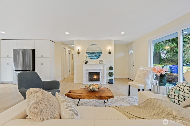 living area featuring light wood-type flooring, a premium fireplace, baseboards, and recessed lighting