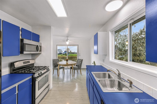 kitchen featuring light wood-style flooring, ceiling fan, appliances with stainless steel finishes, blue cabinets, and a sink