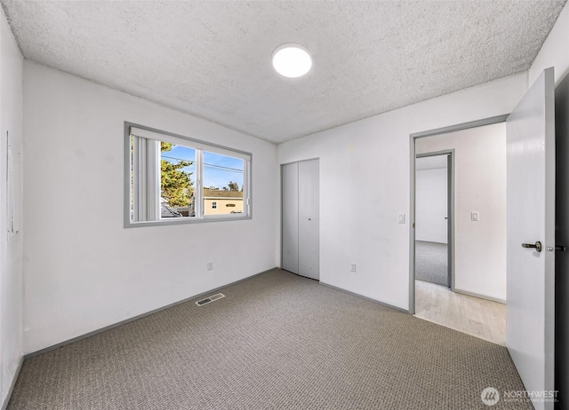 unfurnished bedroom featuring a textured ceiling, visible vents, baseboards, a closet, and carpet