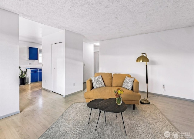 living room with light wood-type flooring, baseboards, and a textured ceiling