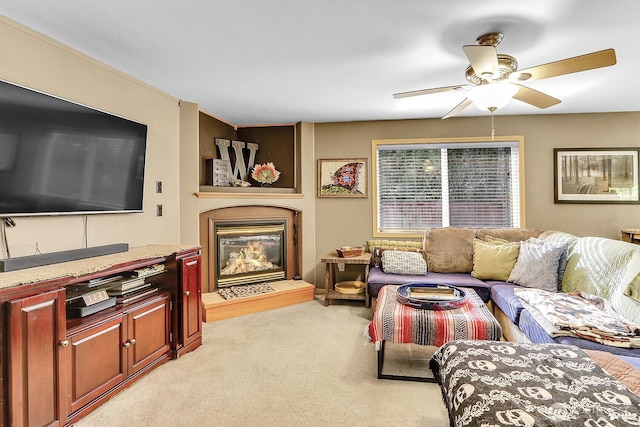 living area with a glass covered fireplace, a ceiling fan, and light colored carpet