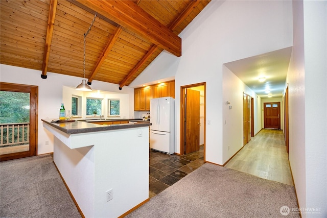 kitchen featuring carpet floors, a peninsula, freestanding refrigerator, dark countertops, and plenty of natural light