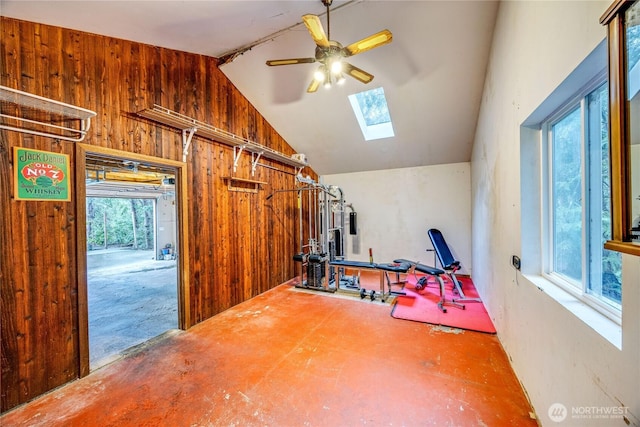 exercise area featuring wood walls, vaulted ceiling with skylight, and ceiling fan