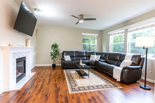 living room with ceiling fan, baseboards, a tiled fireplace, and wood finished floors