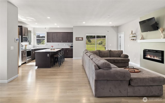 living area with a glass covered fireplace, light wood-style flooring, baseboards, and recessed lighting