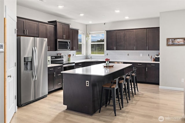 kitchen with light wood-style flooring, appliances with stainless steel finishes, dark brown cabinets, and a breakfast bar area