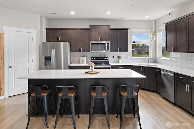 kitchen featuring a breakfast bar, a center island, backsplash, appliances with stainless steel finishes, and a sink