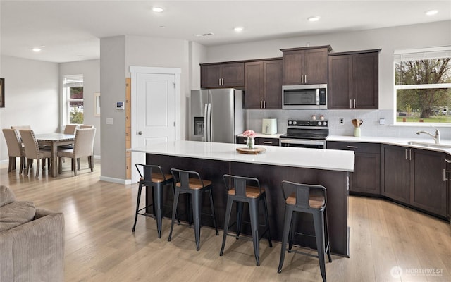 kitchen featuring dark brown cabinetry, tasteful backsplash, appliances with stainless steel finishes, a kitchen breakfast bar, and a sink