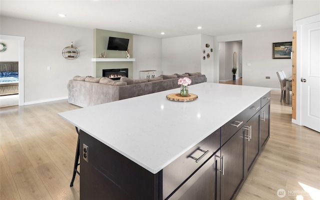 kitchen with a glass covered fireplace, a kitchen island, light countertops, light wood-type flooring, and recessed lighting