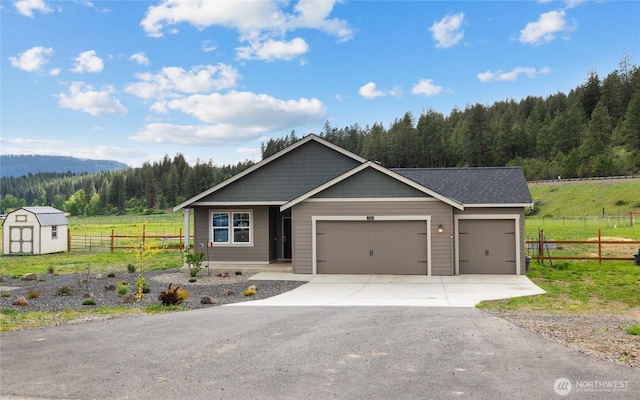 view of front of property featuring an attached garage, driveway, a wooded view, and fence