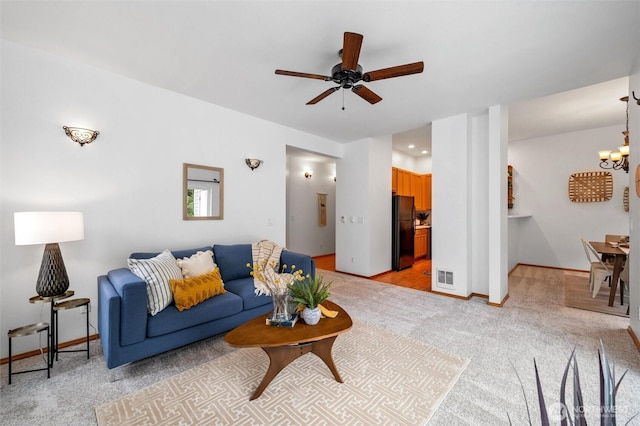 living area featuring baseboards, ceiling fan with notable chandelier, visible vents, and light colored carpet