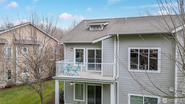 rear view of property with a yard, a shingled roof, and a balcony