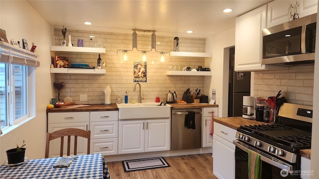 kitchen with wooden counters, open shelves, stainless steel appliances, white cabinetry, and a sink