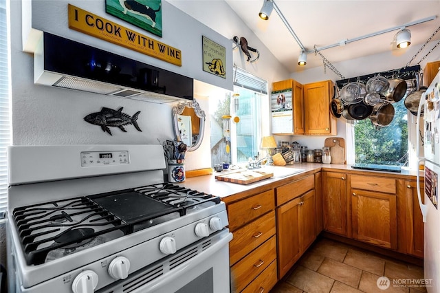 kitchen with gas range, light countertops, lofted ceiling, brown cabinets, and rail lighting