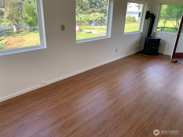 empty room with baseboards, wood finished floors, and a wood stove