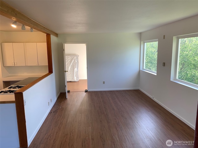 unfurnished living room featuring dark wood-type flooring, beamed ceiling, and baseboards