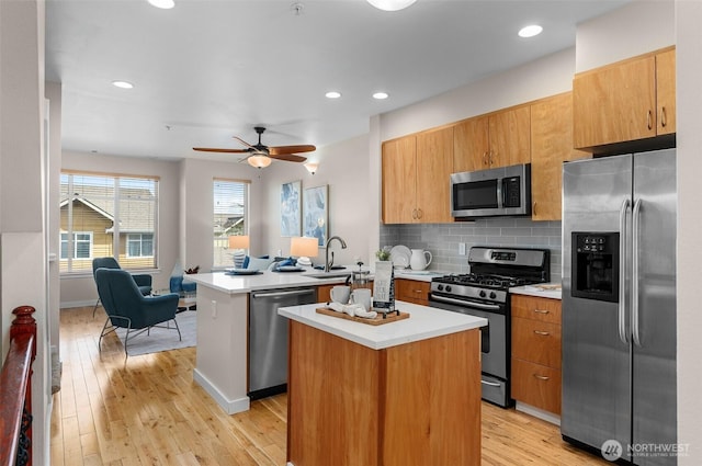 kitchen featuring stainless steel appliances, tasteful backsplash, light countertops, a kitchen island, and a peninsula