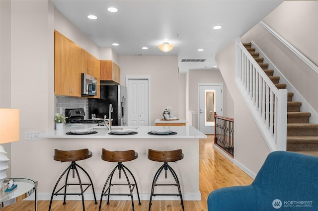 kitchen with a peninsula, visible vents, a kitchen breakfast bar, light countertops, and appliances with stainless steel finishes