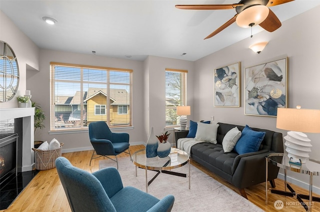 living room with ceiling fan, a fireplace, baseboards, and wood finished floors