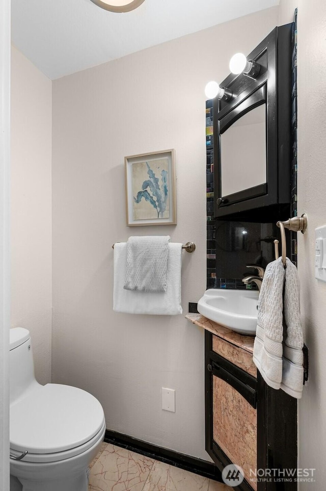 half bathroom with vanity, toilet, and baseboards