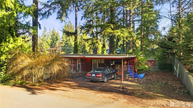 view of front of home with dirt driveway, fence, and a carport