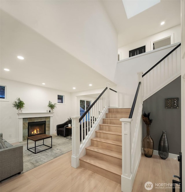 staircase with recessed lighting, a tiled fireplace, and wood finished floors