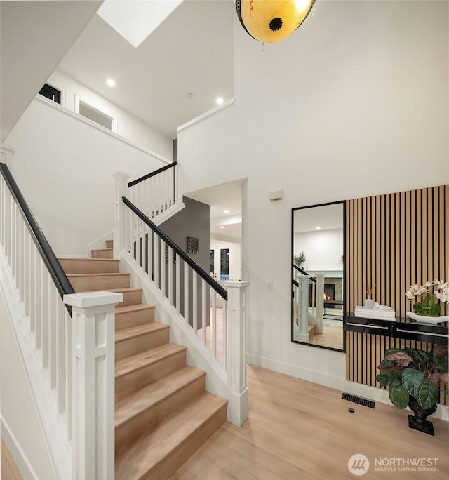 staircase featuring visible vents, a high ceiling, wood finished floors, a warm lit fireplace, and baseboards