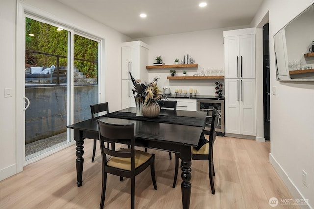 dining room with light wood-style floors, wine cooler, baseboards, and a bar